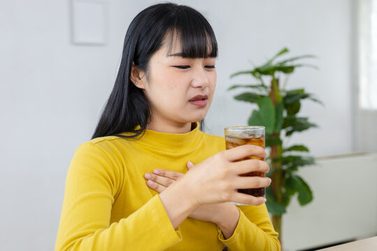 woman feeling chest discomfort while holding glass of soda. Female experiencing heartburn, acid reflux or indigestion after drinking soft drink. Healthcare concept.