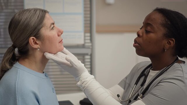African American female healthcare professional performing careful neck palpation to assess glands and lymph nodes as part of patient examination