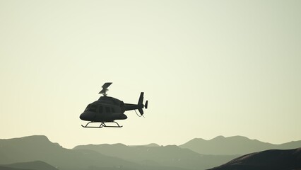 A helicopter glides gracefully over a range of mountains as the sun sets, casting a warm glow across the sky. The silhouette highlights the peacefulness of the evening scene. © icetray
