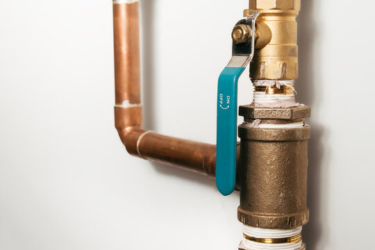Shut-off valve or ball valve on copper pipes. Part of home heating or plumbing system. Controls gas, oil, or water supply safely. For residential or commercial use. Selective focus.