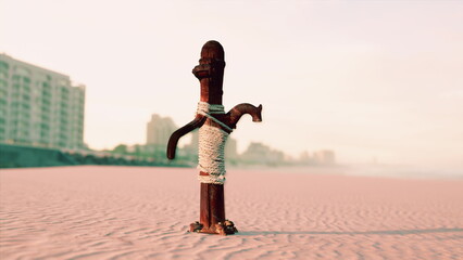A beautifully crafted wooden sculpture stands tall on a sandy beach. The scene captures early morning light, illuminating the structure against a backdrop of distant buildings. © icetray