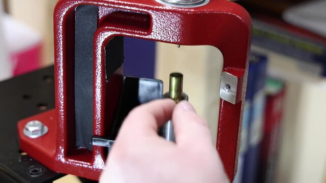 Close-up of a red reloading press with a small black primer catcher and metal components