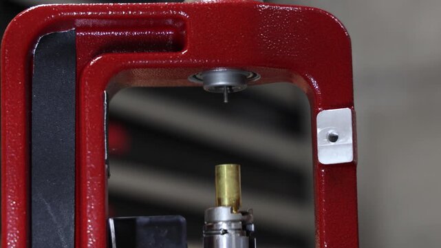 Close-up of a hand adjusting a red reloading press mechanism for precision work