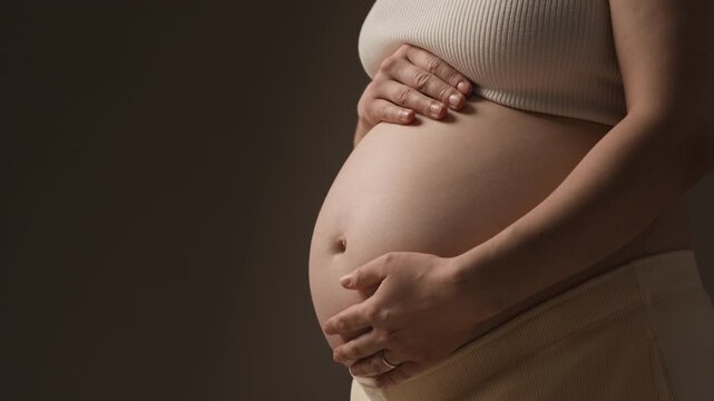 Close up view of baby bump with hands gently resting on belly, highlighting pregnancy, care and prenatal health