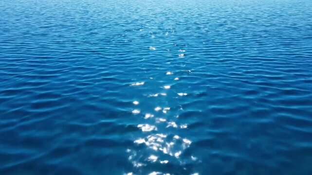 Water moves under sunlight creating a sparkling effect on the surface of a large body of water in an open setting