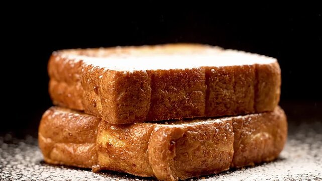 Deliciously prepared golden brown breakfast toast, generously dusted with white powdered sugar, stacked neatly and ready to be enjoyed as a sweet and comforting treat on a dark background
