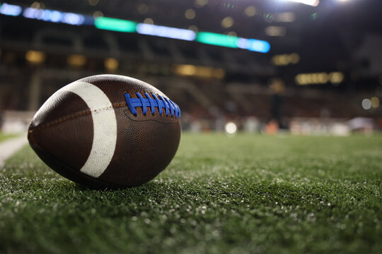 American Football resting on the turf field of a football stadium at night under the stadium lights. Good football concept photo