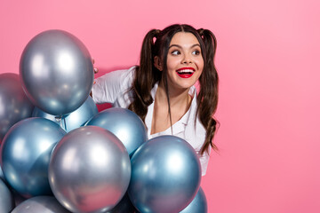Naklejka premium Joyful young woman with blue balloons poses against pink background smiling brightly in a casual summer fashion shoot