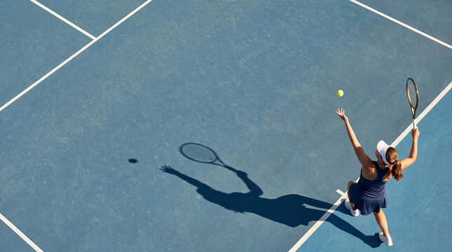 Young female tennis player serving on blue court with strong shadow and motion energy