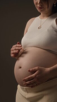 Vertical studio portrait of beautiful young Caucasian expectant mother gently touching bare belly in studio