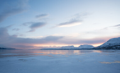 Fototapeta premium Frozen winter landscape near Abisko national park at sunrise, with Lapporten, arctic mountains, and smooth ice