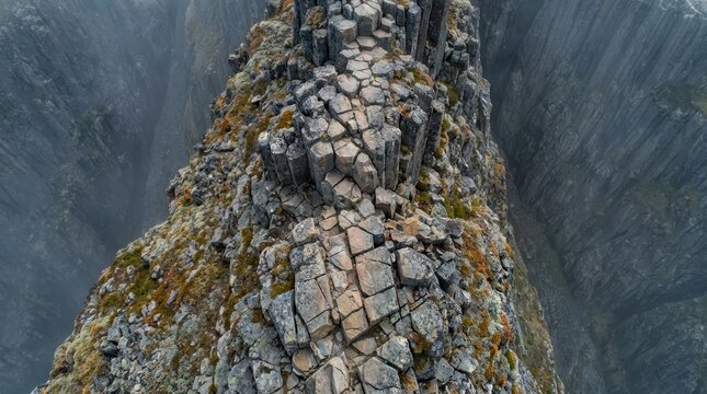 Rugged narrow rocky ridge with distinct hexagonal basalt columns and colorful moss overlooking a deep misty canyon