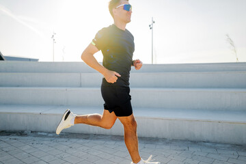 Man runs on a concrete path in bright sunlight near steps during afternoon exercise