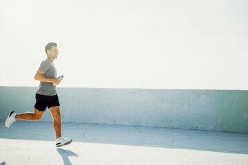 Man runs on a track during early morning with a water bottle in his hand for hydration