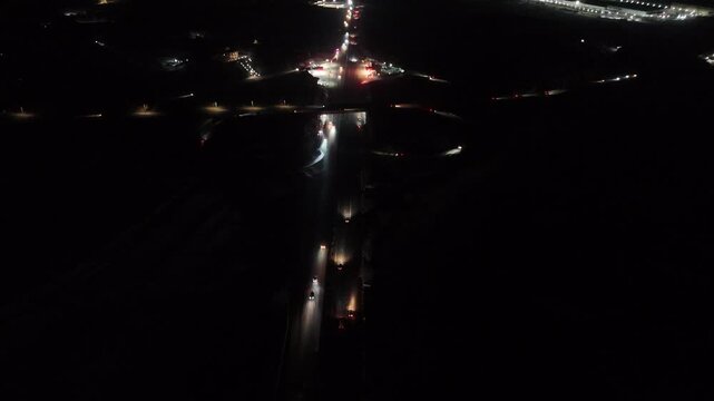 Drone view of illuminated highway intersection at night in low light conditions, infrastructure overview in 4K format.