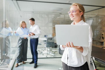 Woman holds laptop while two coworkers discuss in office during daytime