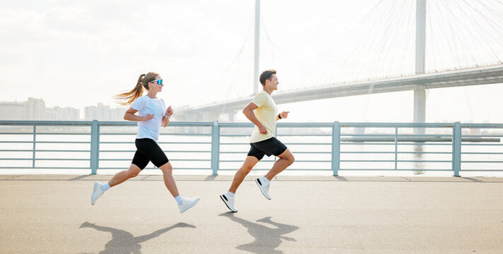 Runners enjoy a morning jog along the waterfront near a bridge in a city