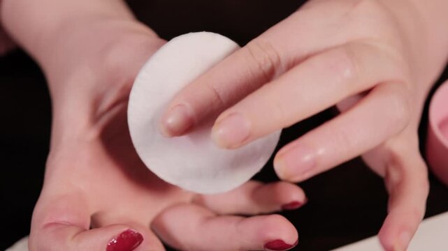 Close up of woman removing red nail polish from fingernails using cotton pad and remover. Detailed manicure correction at home. Beauty routine and self care concept.