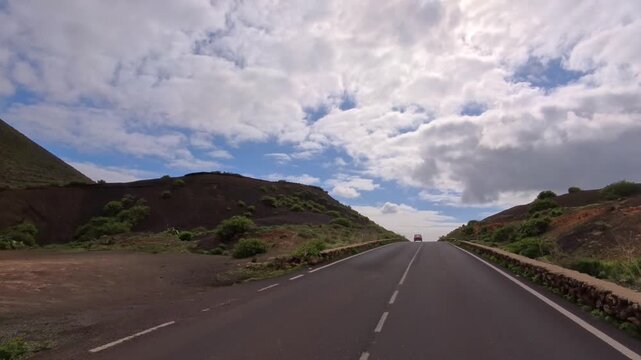 Bergstra&szlig;e auf Lanzarote durch eine gr&uuml;n bewachsene felsige vulkanische Landschaft bew&ouml;lktem Himmel am Horizont, reisen, Roadtrip, Kanarische Inseln, Spanien, bergauf, Urlaub
