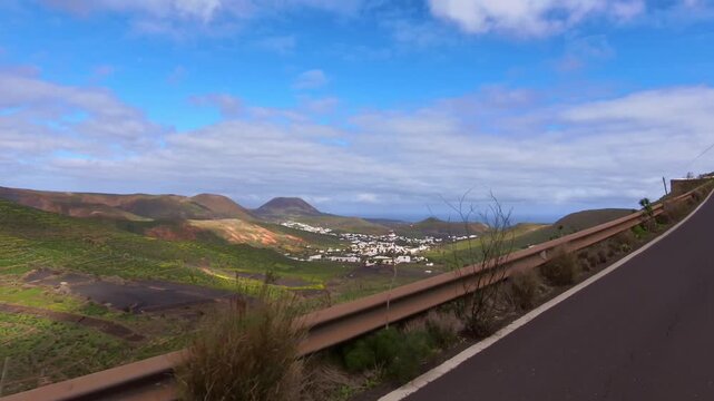 Mountain road on Lanzarote through a green, rocky volcanic landscape with the sea and blue sky on the horizon &ndash; view of the town of Haria,  travel, road trip, Canary Islands, Spain