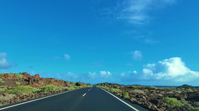 K&uuml;stenstra&szlig;e auf Lanzarote durch eine gr&uuml;n bewachsene felsige vulkanische Landschaft mit Meer und blauem Himmel am Horizont, Freiheit,  Erkundung, reisen, Roadtrip, Kanarische Inseln, Spanien