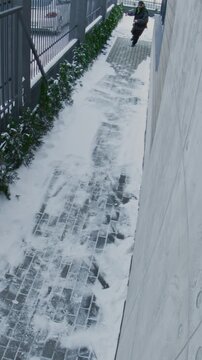 Suspicious Man in Black Cap and Dark Sunglasses Runs Along Pathway, Looking Back While Holding Leather Bag, Captured Outdoor Surveillance Camera. Urgency, Escape, Criminal Behavior. Vertical Shot.