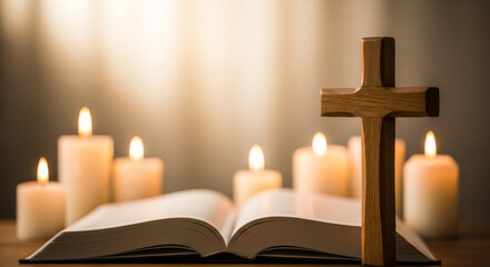 Open Bible beside wooden cross and lit candles in soft light  