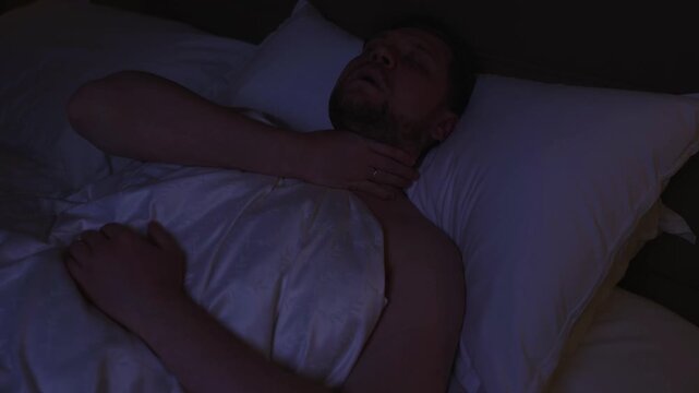 Restless man experiencing breathing problems and sleep apnea symptoms, moving and gasping for air in his bed at night during a stressful nightmare, representing a serious health disorder