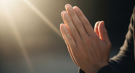 Person with hands together in prayer under soft light  