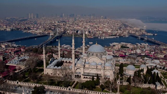 Aerial drone view of S&uuml;leymaniye Mosque in Istanbul, featuring its domes and minarets with the Golden Horn, bridges, boats and historic city skyline in the background.