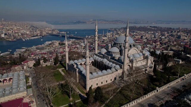Aerial drone view of S&uuml;leymaniye Mosque in Istanbul, featuring its domes and minarets with the Golden Horn, bridges, boats and historic city skyline in the background.