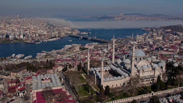 Aerial drone view of S&uuml;leymaniye Mosque in Istanbul, featuring its domes and minarets with the Golden Horn, bridges, boats and historic city skyline in the background.