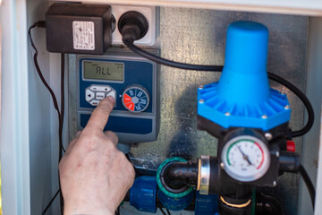 A man hand presses a button on a digital pump controller with a pressure gauge. smart irrigation, water management, garden technology. © Natalia