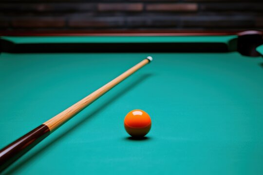 A pool cue is aimed at an orange-striped billiard ball on a green felt pool table.