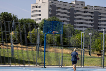 Young man walking on urban basketball court with ball