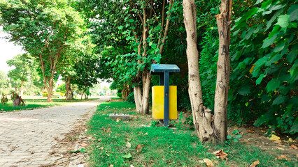 Fototapeta premium Park pathway with trash bin surrounded by trees in clean green area