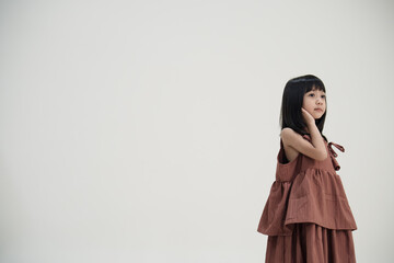 Asian little girl in brown dress touching neck on neutral background, calm children fashion portrait.