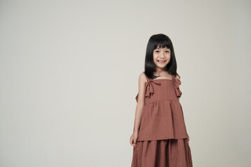 Smiling Asian little girl in brown dress on neutral background, happy children fashion portrait.