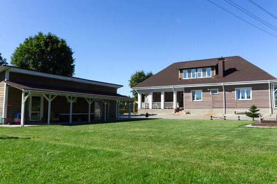 Residential house with porch lawn and wooden structures under clear blue sky. Well maintained countryside home with porch carport and wooden annex ideal for real estate architecture lifestyle.