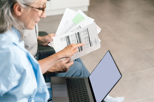 Senior couple reviewing bills and financial documents at home on a laptop