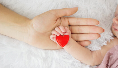 Mother holding hand of newborn baby with red heart, concept of love, care and family