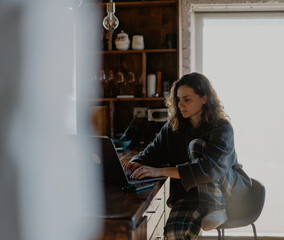 Young woman working on laptop at kitchen table in the morning at home