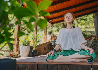 Young blonde woman practicing yoga and meditation on a sunny summer terrace.