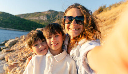 Happy mother with two twin sons 10 years old enjoying summer vacation on sea beach. Selfie