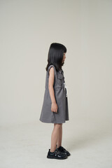 Side view full body Asian girl in gray dress on neutral background, children fashion profile portrait. © Rangga Ispraditya