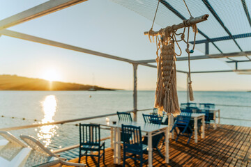 Empty outdoor cafe on wooden pier at sea during sunrise golden hour