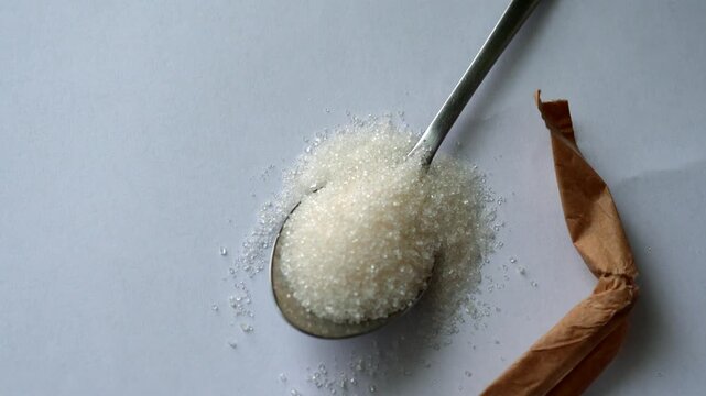 A teaspoon of sugar in the kitchen.
A close-up of a sugar stick and a metal kitchen utensil.