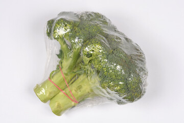 High angle shot of a fresh green broccoli head wrapped in clear plastic film with a red rubber band on a plain white background.