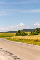 A beautiful, sunny day with a clear blue sky. The sky is dotted with clouds, and the sun is shining brightly. The scene is peaceful and serene, with a large field of grass and trees in the background