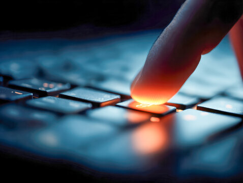 Finger pressing illuminated key on keyboard with glowing orange light in dark setting representing technology and digital interaction concept